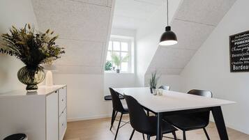 A modern dining area with a white table, black chairs, a pendant light, and a decorative plant.