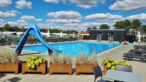 A swimming pool with a blue slide, lounge chairs, and planters with greenery. - Ribe Camping (Ribe)
