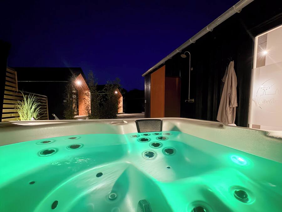 Un jacuzzi con múltiples chorros, rodeado de un moderno entorno exterior con una casa y un jardín.