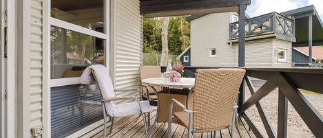 Un patio techado al aire libre con una mesa y sillas, un ventanal corredizo y vistas a casas vecinas.