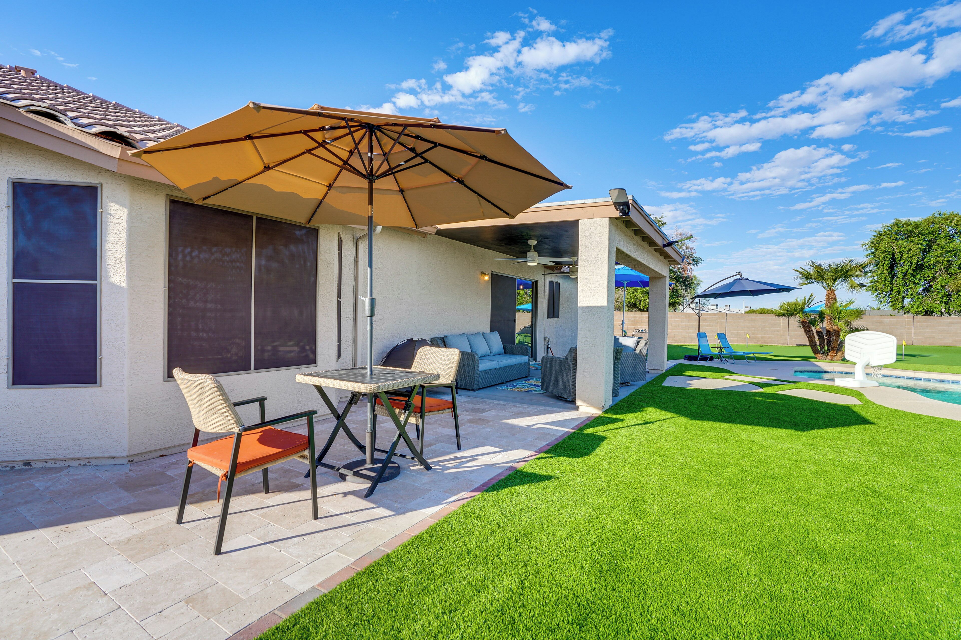 Een terras met een tafel, stoelen, een grote parasol en een zwembad.
