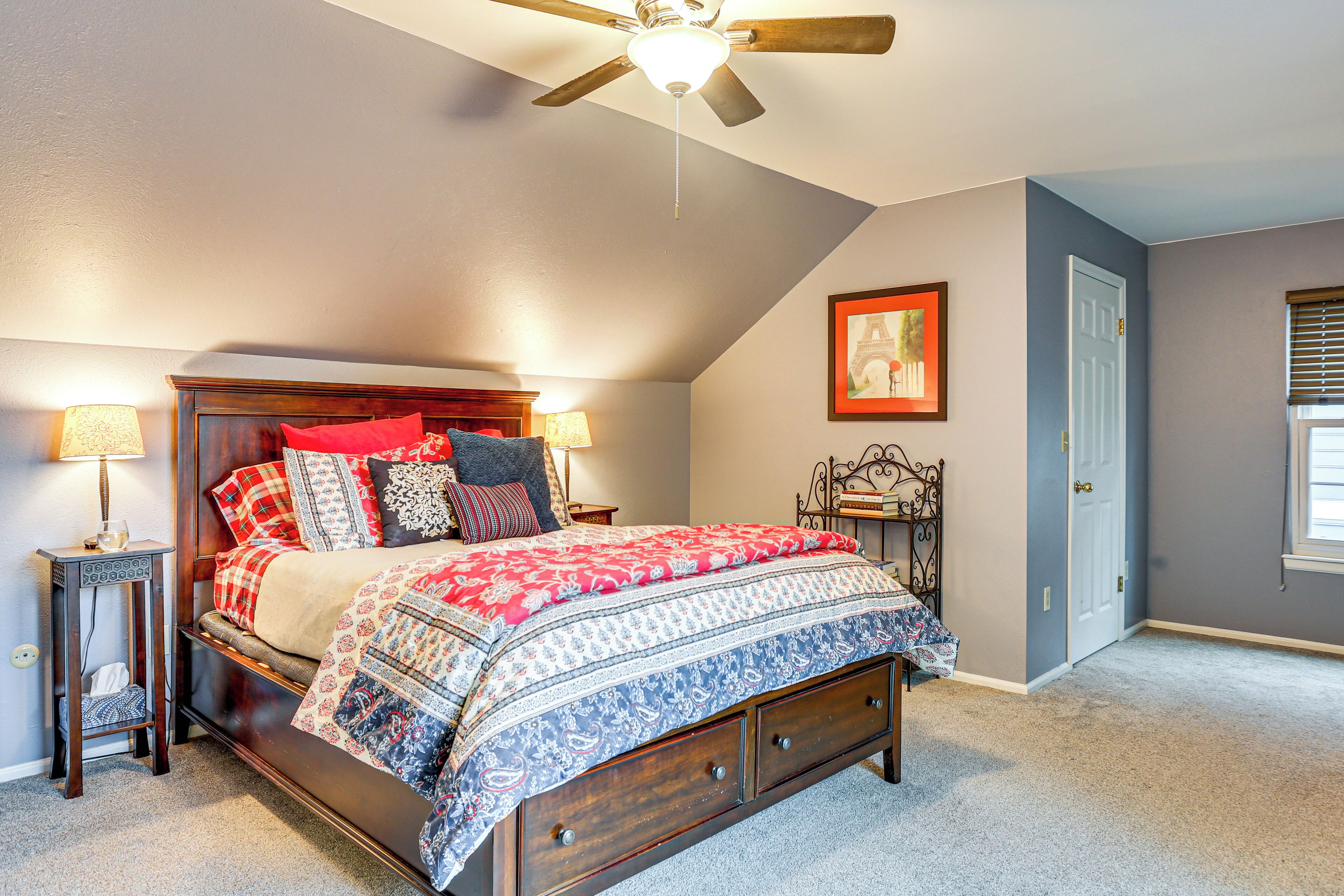 A bedroom with a wooden bed, a ceiling fan, two bedside tables with lamps, a door, and a window with blinds.