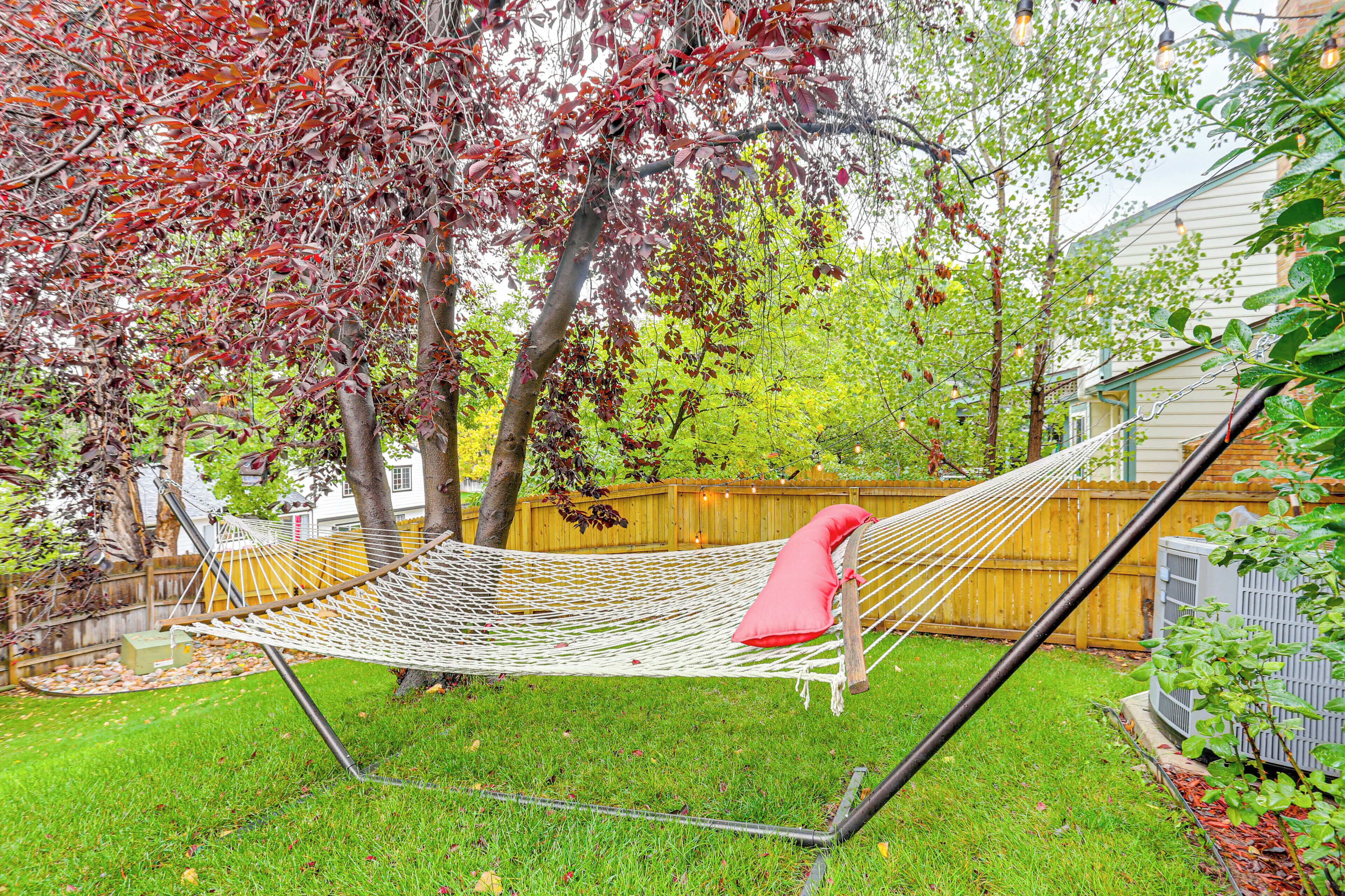 A hammock in a backyard with a wooden fence, a tree, and a house in the background.