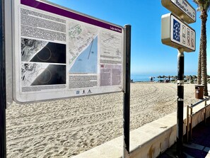 A beachside informational sign with maps and text, a palm tree, and a clear sky. - Belvilla by Oyo Luxury Tropicana Club (Roquetas de Mar)