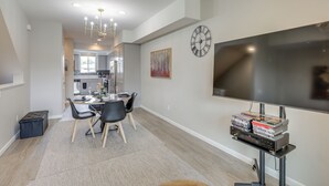 A modern living room with a flat-screen TV, a dining area with a table and chairs, and a kitchen in the background. - Home Base w/ Easy 1-80 Access: 4 Mi to Dtwn Reno! (Reno)