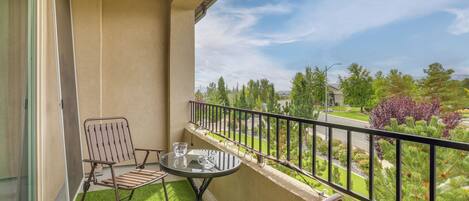 A balcony with a table and chairs, a view of a landscaped garden, and a clear sky.