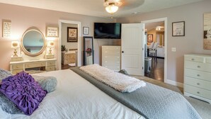 Une chambre à coucher avec un grand lit, une commode, une coiffeuse avec un miroir, un téléviseur et un ventilateur de plafond.