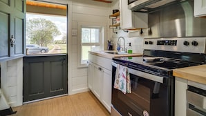 A kitchen with a large stove, a sink, and a window overlooking a driveway. - Cozy Couples Retreat w/ Porch on Bayou Teche! (New Iberia)