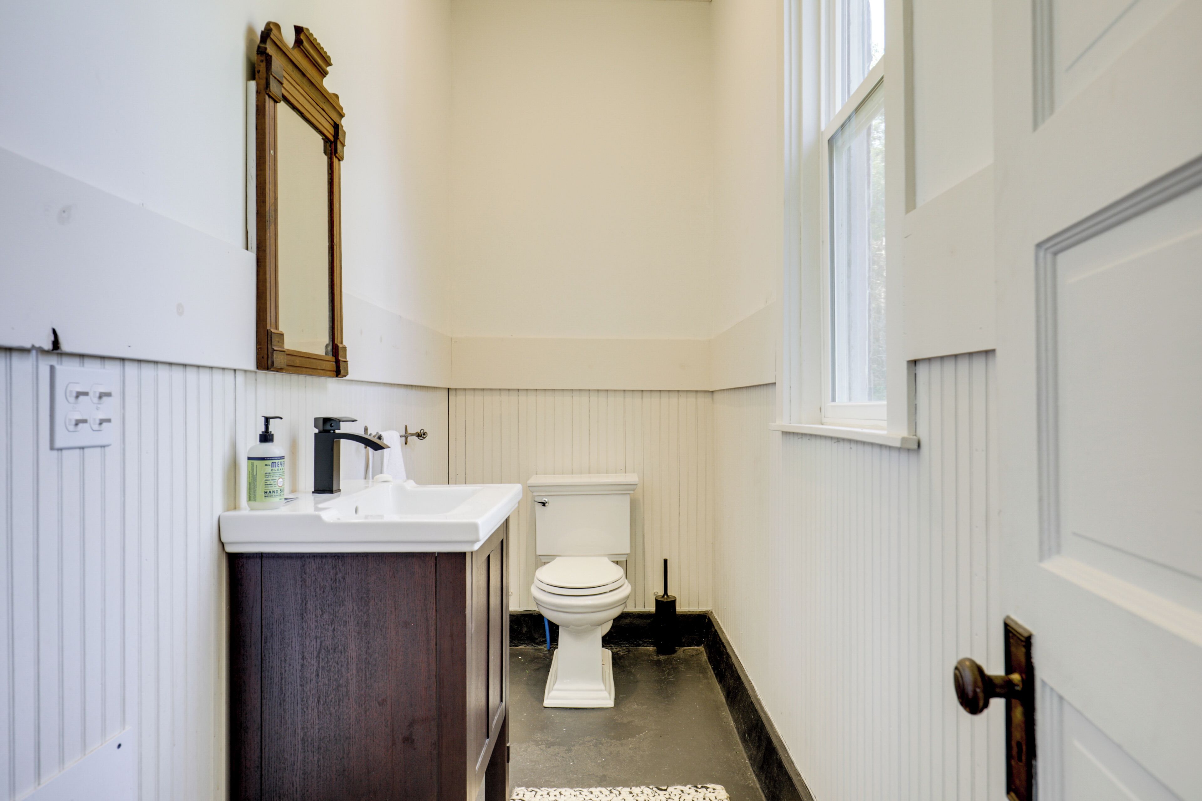 A bathroom with a white toilet, a wooden vanity, a mirror, and a window.