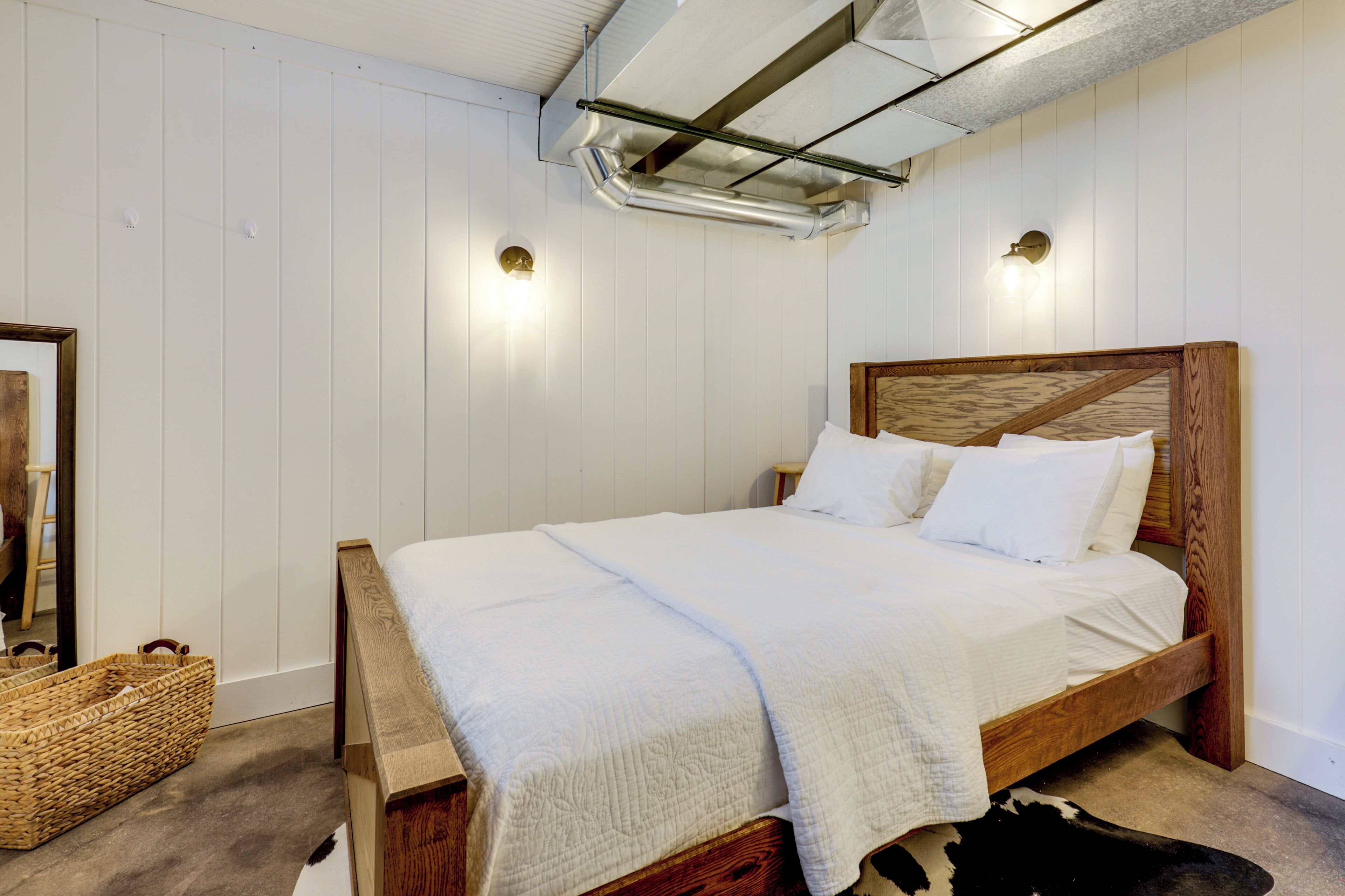 A bedroom with a wooden bed, white bedding, a woven basket, and a cowhide rug.