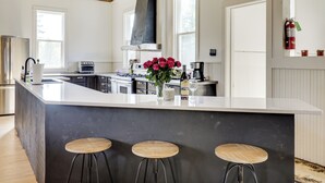 A modern kitchen with a large island, bar stools, and a vase of flowers. - 'the Townhall' Northwoods Retreat w/ Large Patio! (Conover)