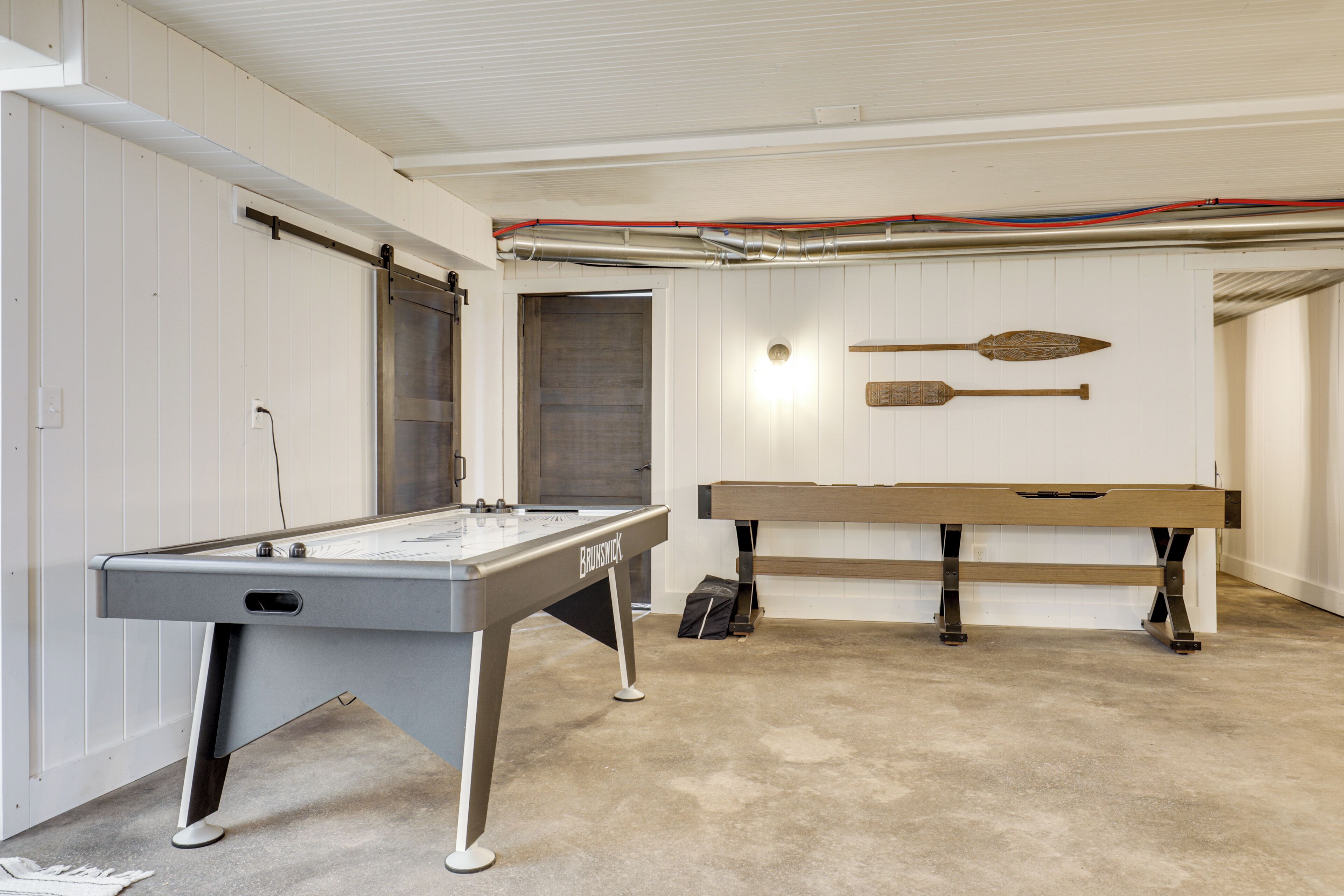 A pool table with a billiard cue and a dartboard in a room with white walls and a concrete floor.