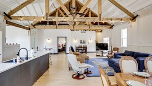 A spacious living area with a high ceiling, wooden beams, a dining table set for four, a sofa, and a TV in the background. - 'the Townhall' Northwoods Retreat w/ Large Patio! (Conover)
