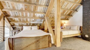 A wooden-framed attic bedroom with a bed, a small table, and a brick wall. - 'the Townhall' Northwoods Retreat w/ Large Patio! (Conover)
