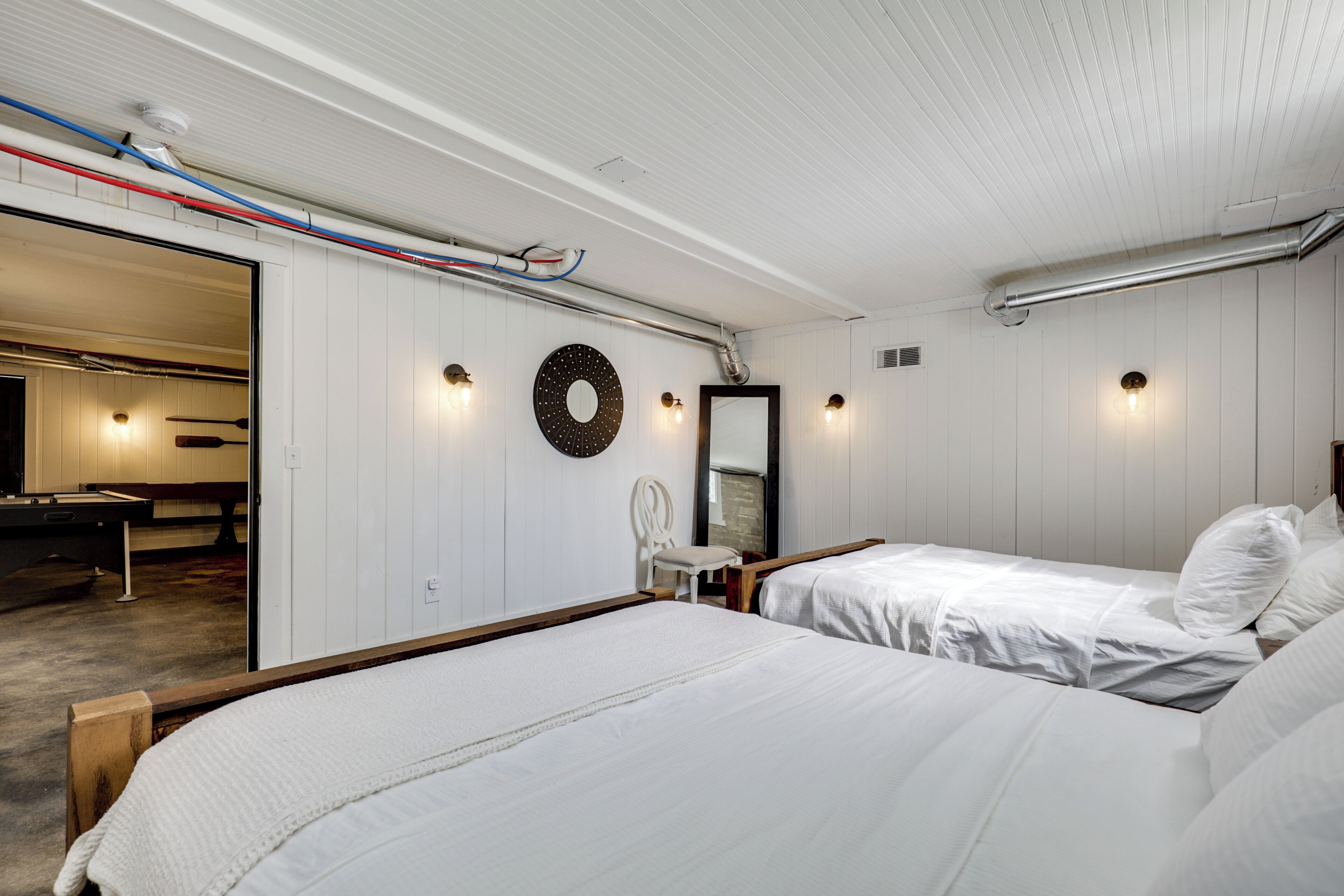 Une chambre d’hôtel avec deux lits, un bureau, une chaise, un miroir rond et un anneau lumineux fixé au mur.