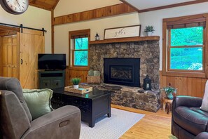 A cozy living room with a stone fireplace, wooden beams, a television, and leather sofas.