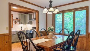 A dining area with a wooden table, black chairs, a chandelier, and a view of the outdoors through large windows. - Hot Tub, Fish, Ski: Outdoorsy Retreat in Boone! (Vilas)