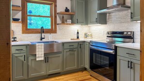 A kitchen with light green cabinets, a stainless steel range, a built-in oven, a window with a view, and a wooden ceiling. - Hot Tub, Fish, Ski: Outdoorsy Retreat in Boone! (Vilas)