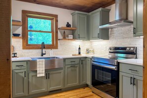 A kitchen with light green cabinets, a stainless steel range, a built-in oven, a window with a view, and a wooden ceiling.