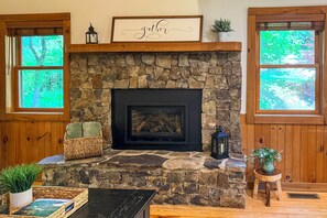 A stone fireplace with a framed sign above, a wicker basket, and a small table with a plant.