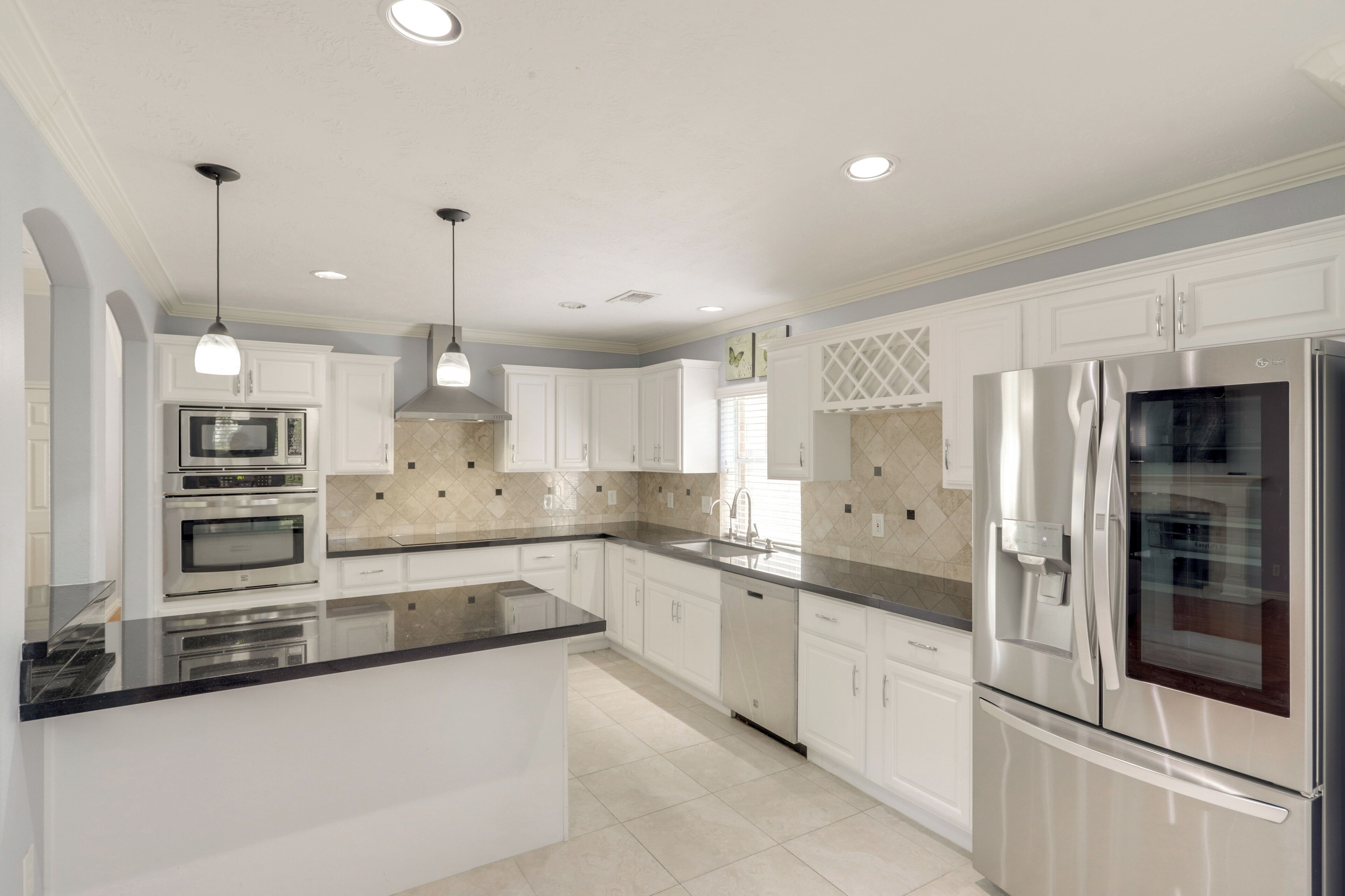 A modern kitchen with white cabinetry, stainless steel appliances, and a black countertop island.