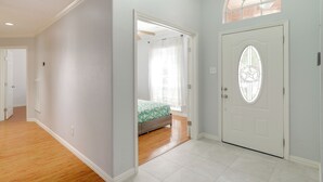 Un pasillo que conduce a un dormitorio con una cama, una puerta con un panel de vidrio decorativo y una ventana con vistas al exterior.