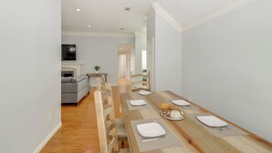 Un comedor con una mesa de madera dispuesta para cuatro personas, un sofá gris al fondo y un pasillo que conduce a otra habitación.