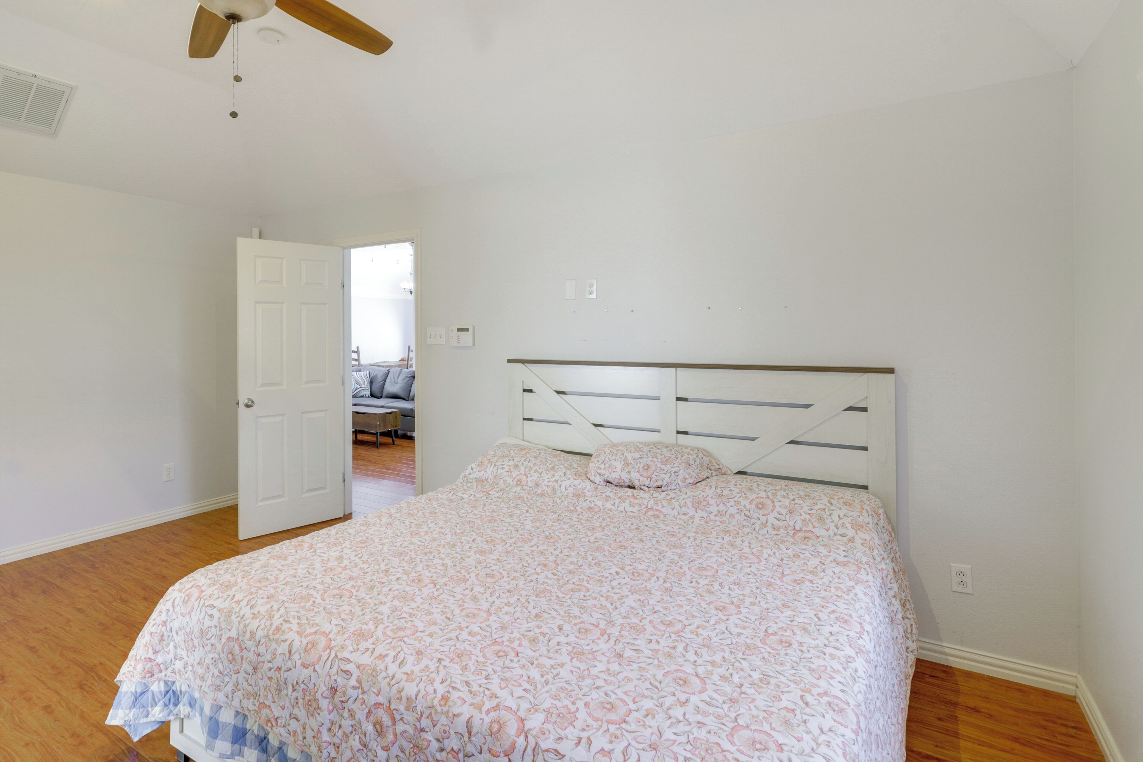 Een slaapkamer met een bed, houten vloeren, een plafondventilator en een deur naar een andere kamer.