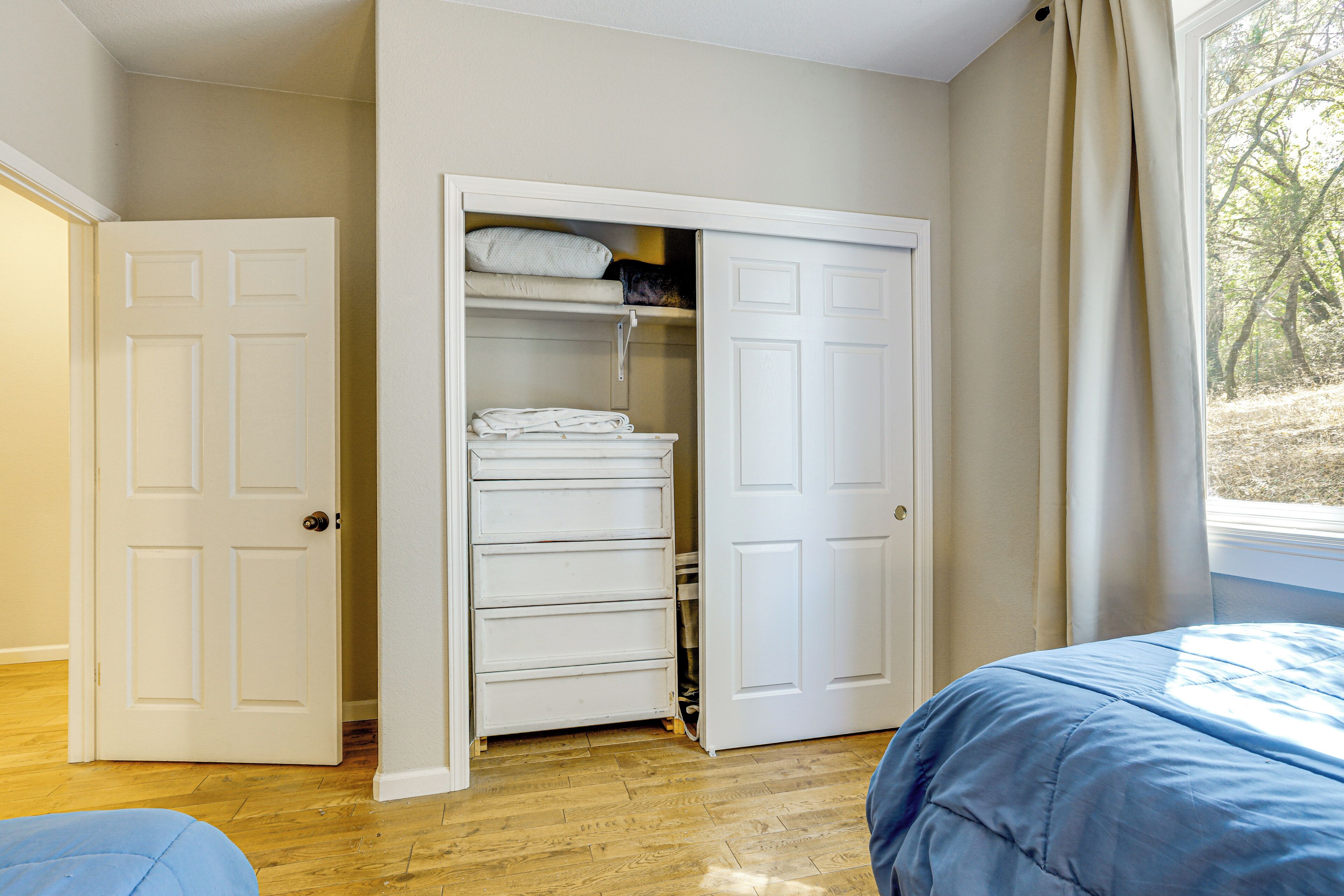 A room with a bed, a wardrobe, and a window with a view of trees.