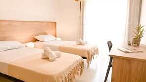 A hotel room with two beds, a wooden headboard, a desk with a plant, and a window with curtains.