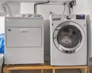 Two white laundry machines, one with a front-loading door and the other with a top-loading door, placed on a wooden platform.
