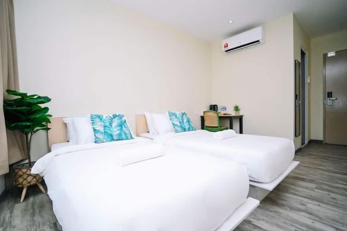 Een hotelkamer met twee bedden, een klein tafeltje met een plant en een airconditioning aan de muur.