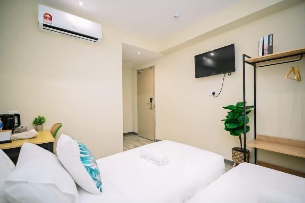 Hotelkamer met twee bedden, een flatscreen televisie, een koffiezetapparaat, een plant en een plank met boeken.