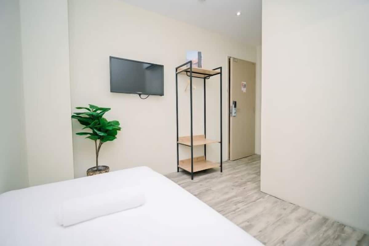 Een hotelkamer met een bed, een aan de muur bevestigde televisie, een plant en een houten plankunit.