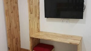 Eine Ecke mit einer hölzernen Bank, einem roten Kissen und einem an der Wand befestigten Fernseher.