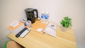 Ein Holztisch mit einer schwarzen Kaffeemaschine, zwei Wasserflaschen, einer Fernbedienung, einer Tasche für Taschentücher, einer Kissenhülle und einem kleinen Topfpflanzen.