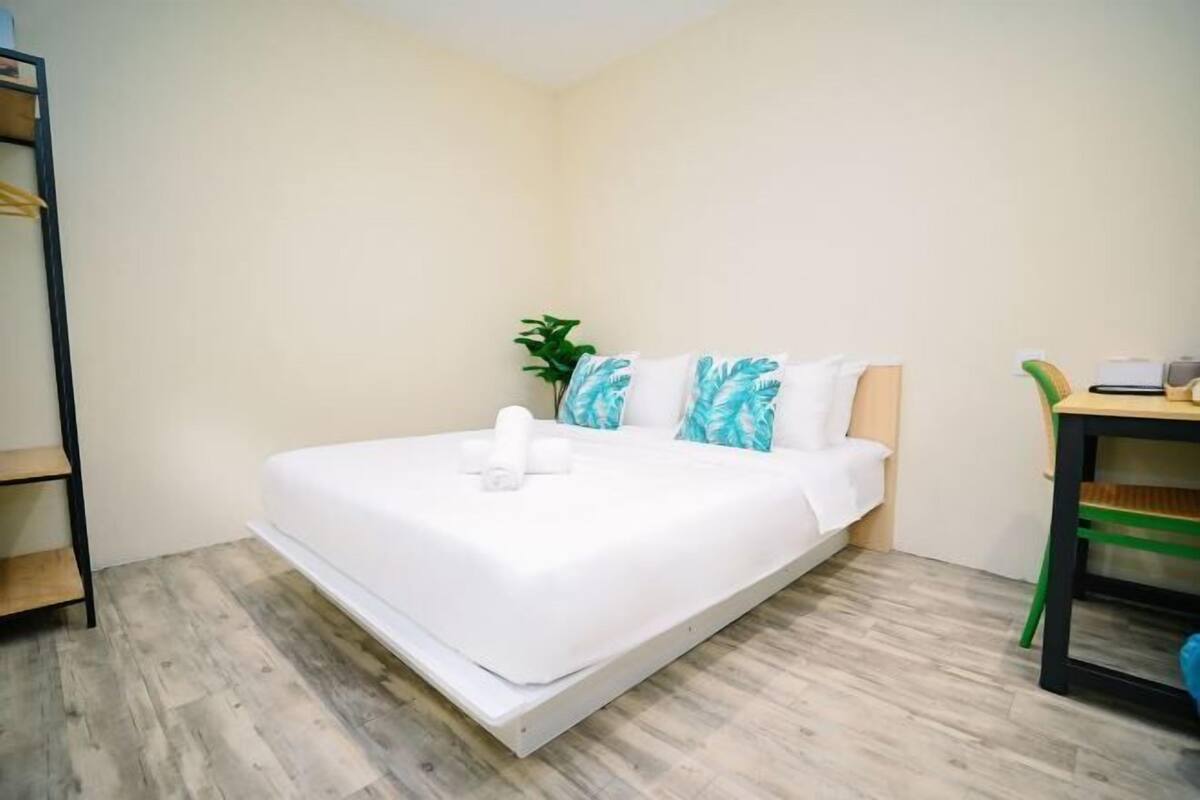 Een eenpersoonsbed met een witte matras en kussens, een klein nachtkastje met een lamp en een groene stoel.
