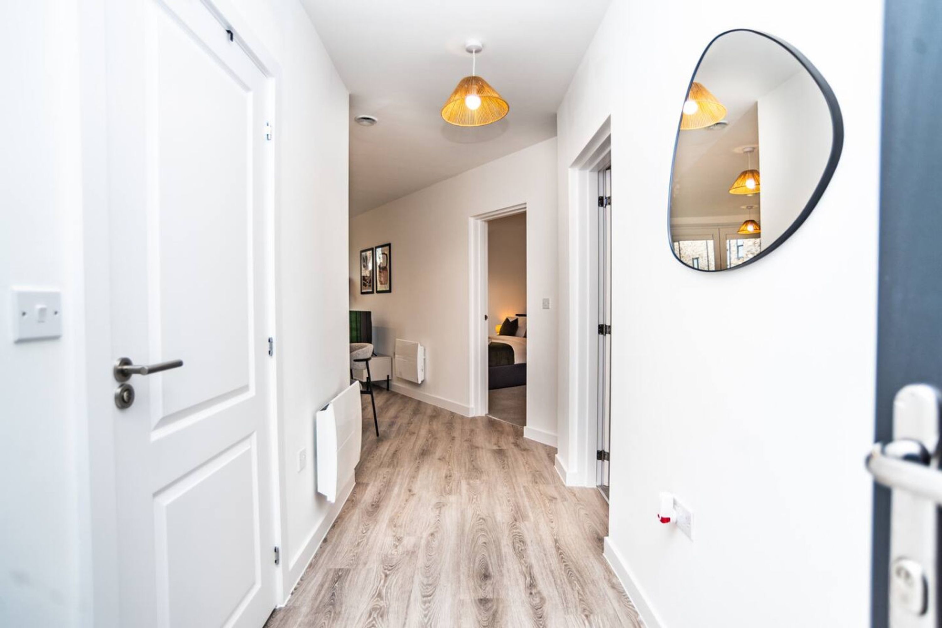 A hallway with a wooden floor, white walls, and a round mirror on the right.