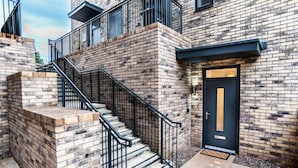 A multi-story building with a brick facade, a black metal staircase, and a black door with a window.