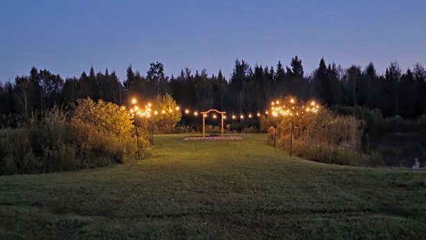 A grassy outdoor area with a wooden pergola and string lights. - Gather Here: 3,000 Sq Ft Lodge in Michigan's U.P. – Pond, Fire, Sleeps 14 (Wilson)