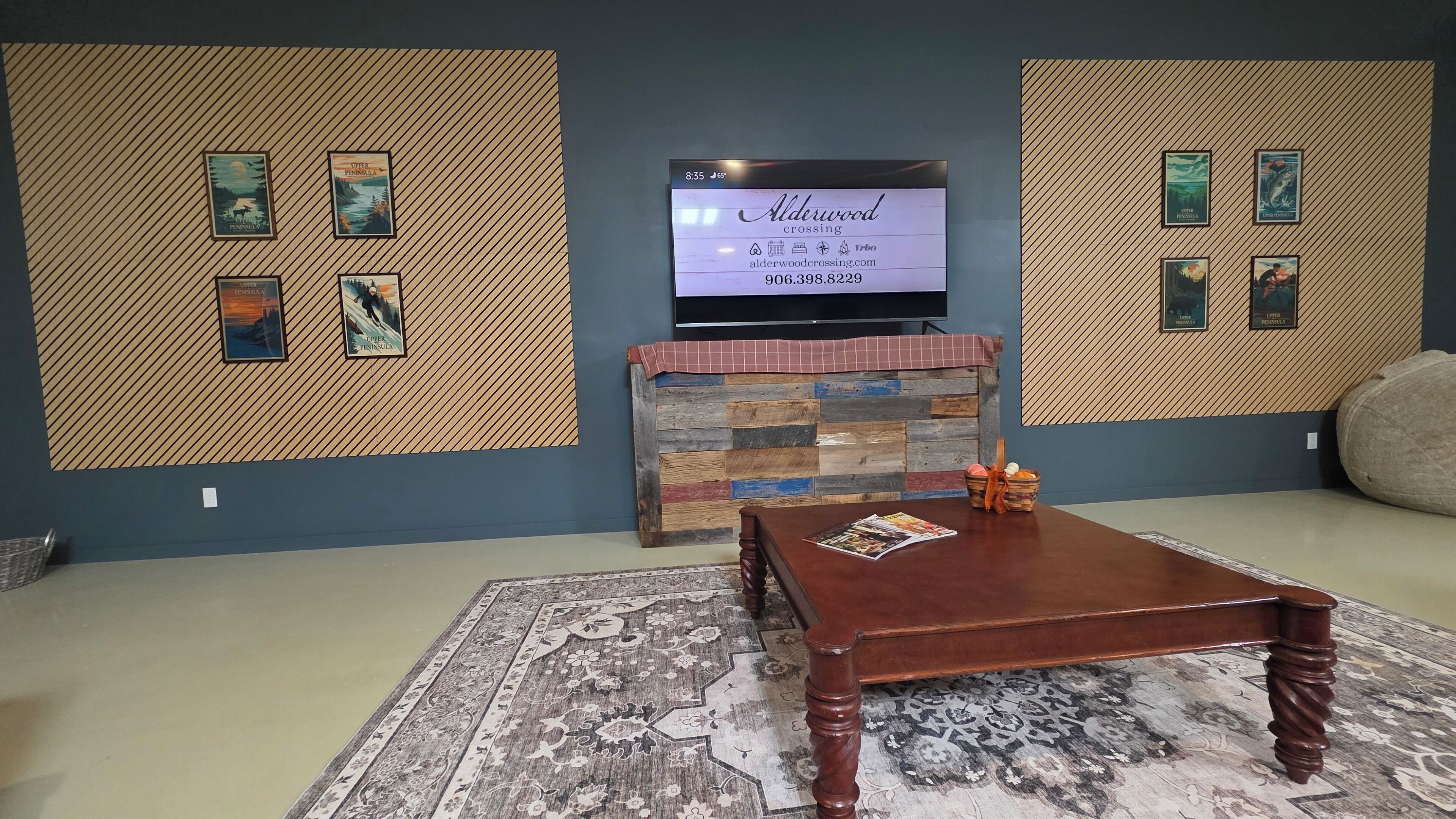 A living room with a television mounted on a wall, a wooden coffee table, a patterned rug, and a small decorative basket.