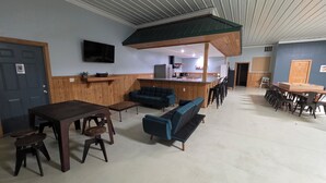 A spacious room with a wooden dining table, blue sofas, and a kitchen area in the background. - Gather Here: 3,000 Sq Ft Lodge in Michigan's U.P. – Pond, Fire, Sleeps 14 (Wilson)