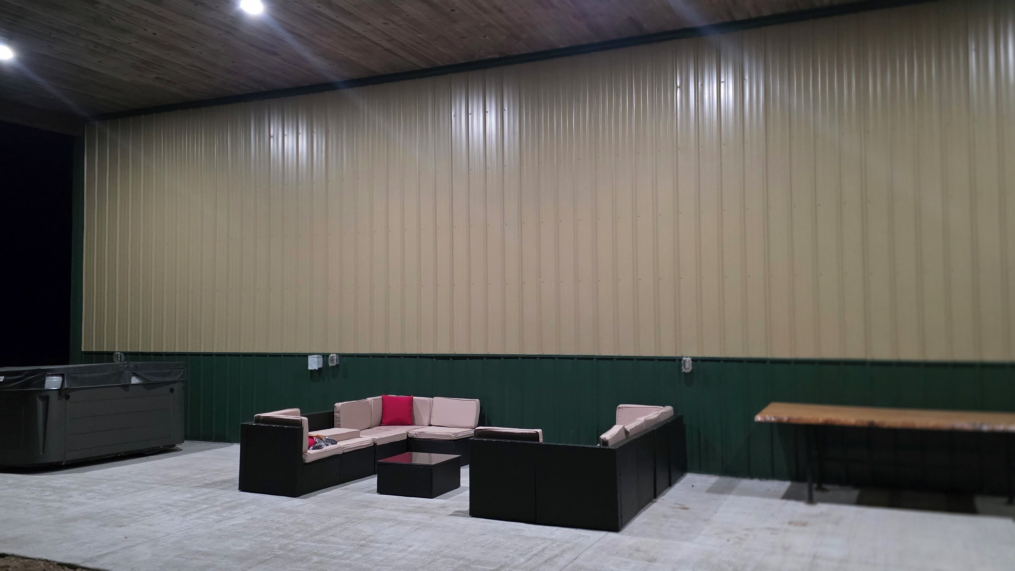 An indoor space with a high ceiling and a green wall. There are two black sofas with cushions, a small table, and a bench.