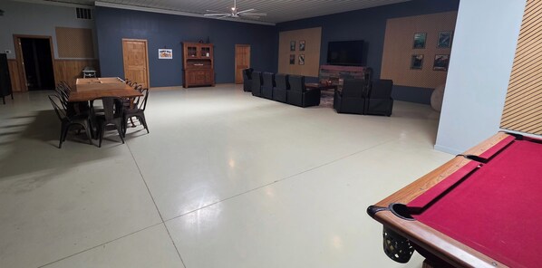 A spacious room with a pool table, a dining area with chairs, and a seating area with sofas.