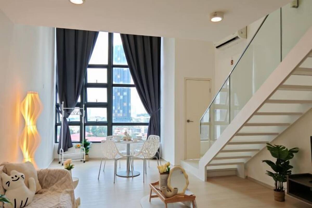 A modern hotel room with a dining area, a staircase, and a view of the cityscape.