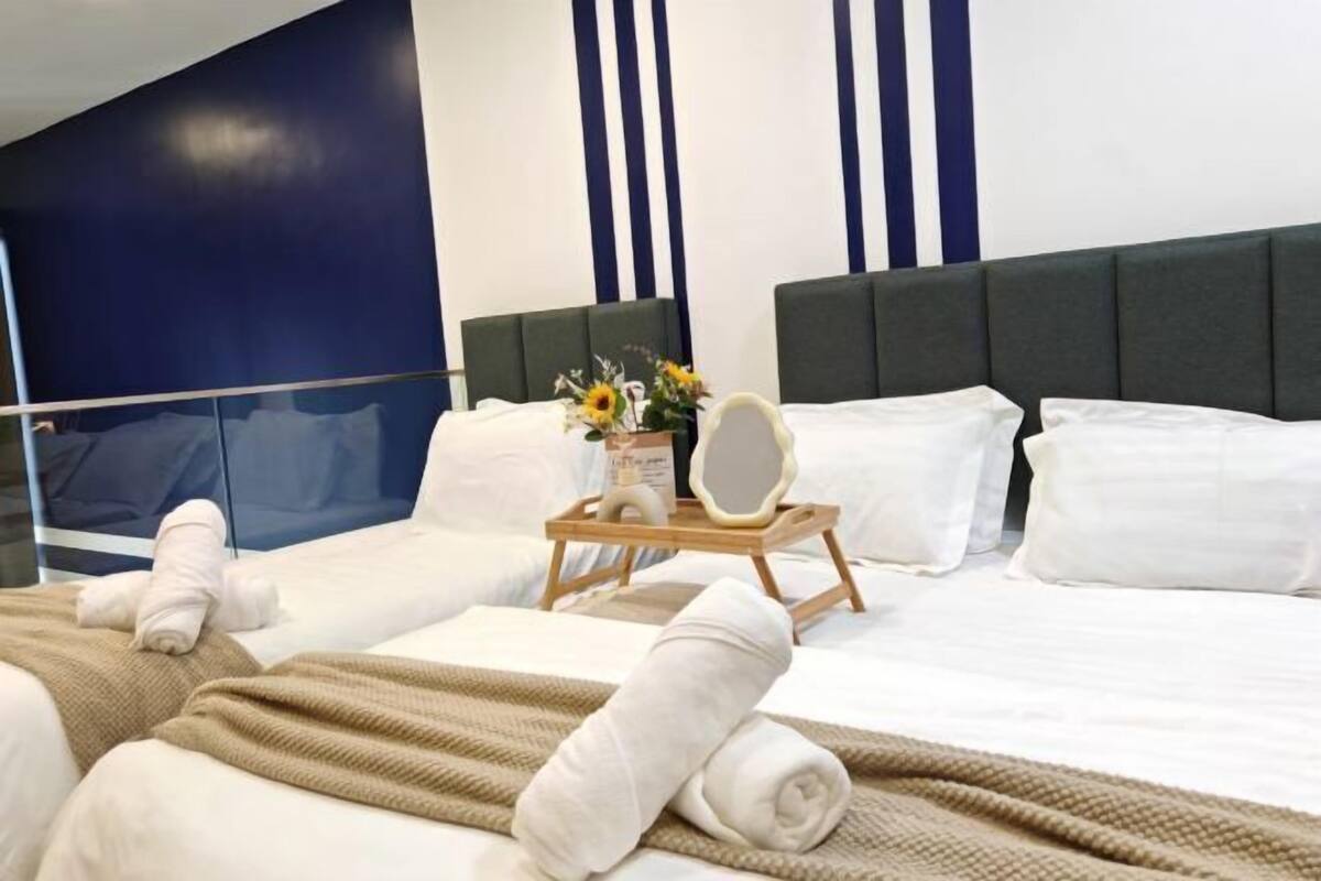 A hotel room with a bed, a bedside table with a mirror, and a tray with towels and a vase of flowers.
