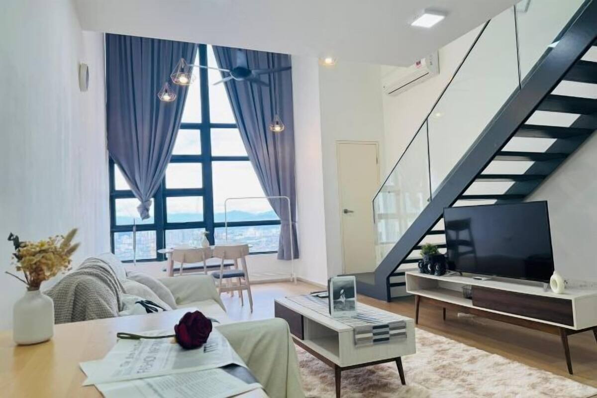 A modern living room with a large window, a flat-screen TV, a staircase, and a dining area.