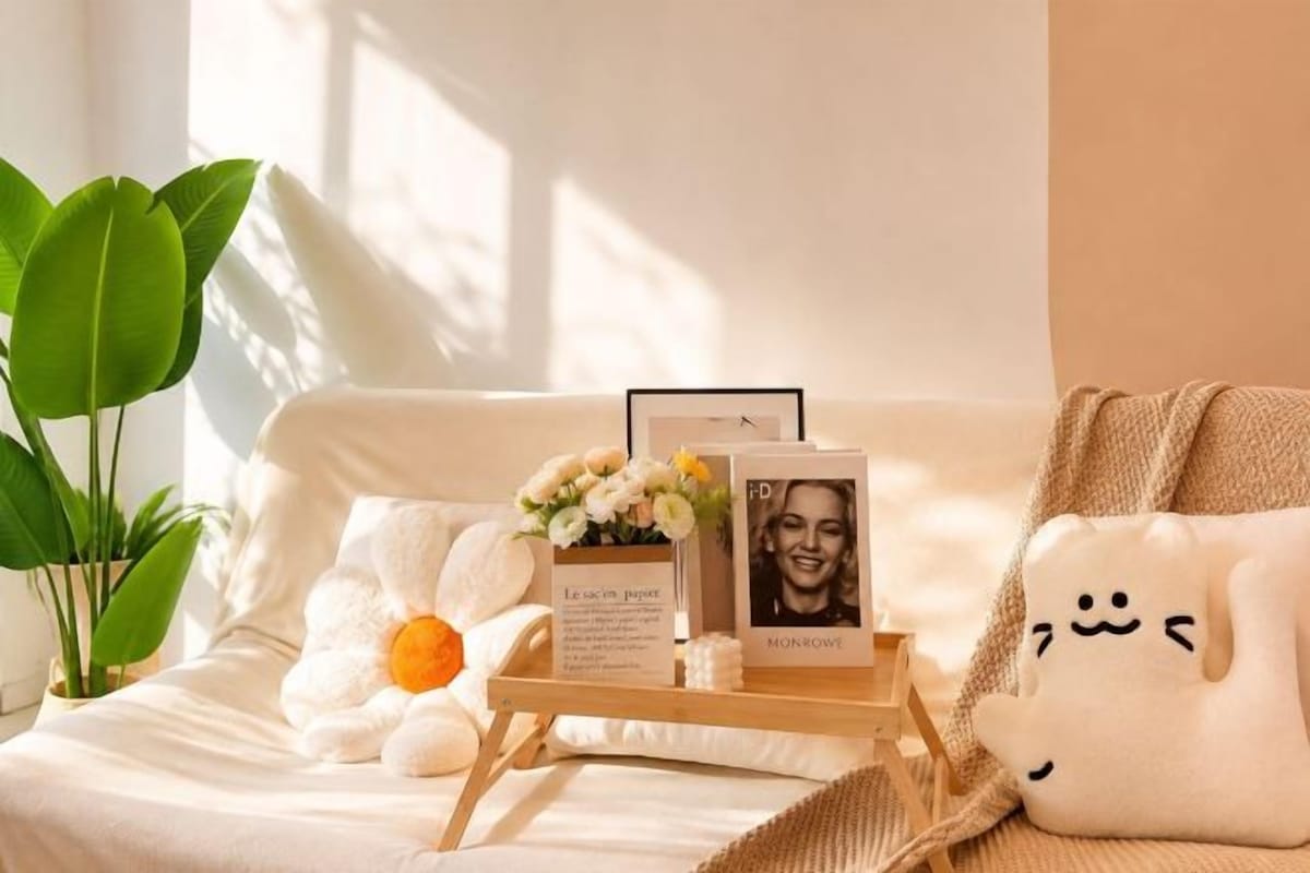 A cozy room with a bed, a bedside table with a photo frame, a plush pillow, and a potted plant.