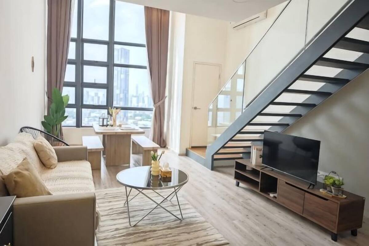 A modern living room with a sofa, coffee table, TV, and a staircase.