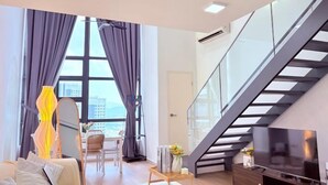 A modern living room with a sofa, a TV, a staircase, and a large window with curtains. - Urban Loft: MRT Convenience, KLCC Nearby @ Eko Cheras (Kuala Lumpur)